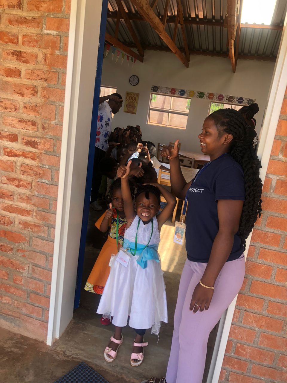 A delighted child gives a thumbs up at the classroom door