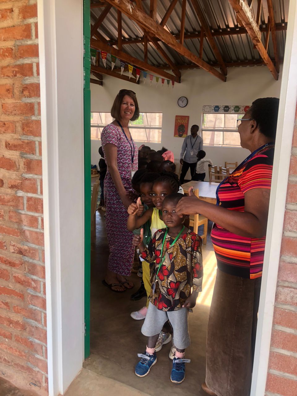 A staff member welcomes smiling children at the classroom entrance